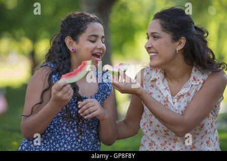 Felice madre ispanica con sua figlia teenager mangiando anguria in posizione di parcheggio Foto Stock