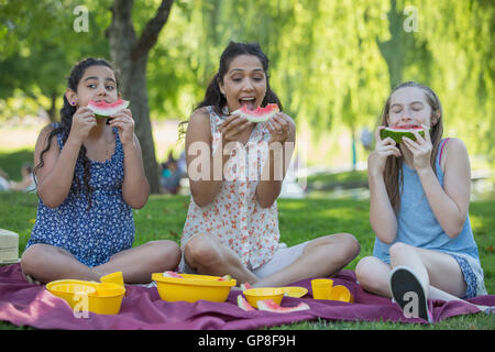 Felice famiglia ispanica avente un picnic e mangiando anguria in un parco Foto Stock