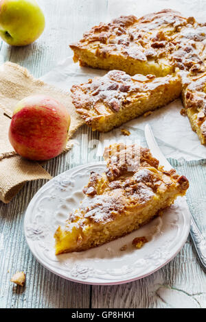 In casa mela e mandorla dolce. Pezzo di torta sulla piastra bianca e frutta fresca su sfondo di legno Foto Stock