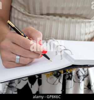 Imprenditrici titolari di un blocco appunti e scrivere su di esso. Close-up di mani femminili. Foto Stock