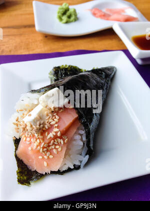 Mano di sushi roll riempita con salmone crudo, riso, crema di formaggio e semi di sesamo di fronte lo zenzero con wasabi e salsa di soia. Japane Foto Stock