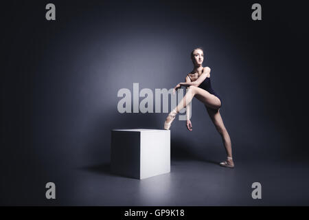 Giovane ballerina in un vestito nero è in ballo nel buio studio Foto Stock