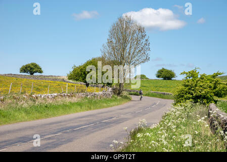 Ciclista su strada di un paese su una bella giornata d'estate nella campagna inglese. Foto Stock