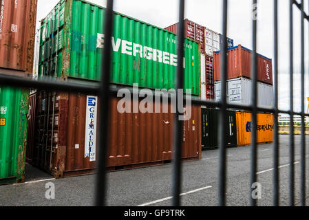 I contenitori di spedizione impilati fino a Belfast Harbour, dietro un muro di sicurezza. Foto Stock