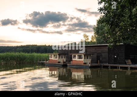 Il panorama su un lago con alberi e canneti e boatshouse Foto Stock