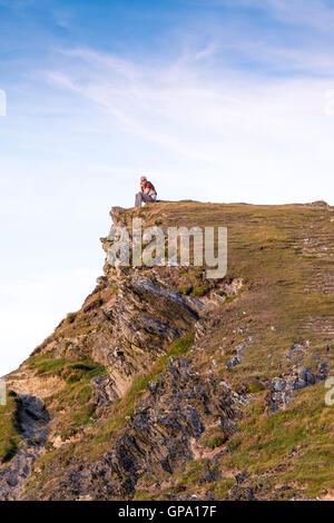 Una donna si siede sul suo proprio sul vertice della testa Trevelgue in Newquay, Cornwall. Foto Stock