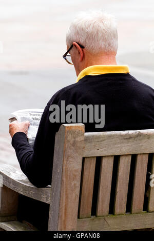 Un anziano uomo seduto su un sedile di estate leggendo un giornale nel centro di Dundee, Regno Unito Foto Stock