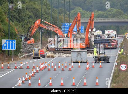 Lavoratori di demolizione di rimuovere la restante struttura del danneggiamento di una passerella oltre l'autostrada M20 nel Kent, che è stata chiusa in entrambe le direzioni per consentire le autostrade in Inghilterra per svolgere il lavoro. Foto Stock