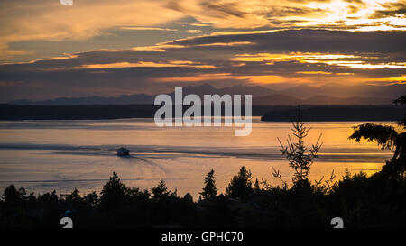 Un traghetto si sposta verso le montagne olimpiche come il sole tramonta su Puget Sound Foto Stock