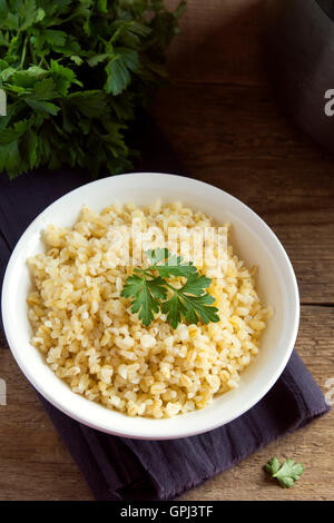 Organici di Bulgur di grano in bianco ciotola close up, sano cibo vegetariano Foto Stock