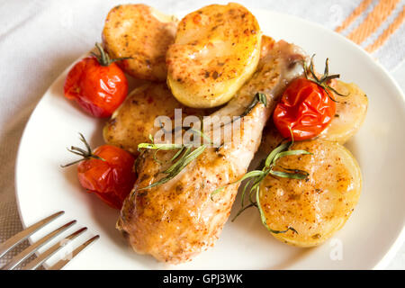 Cotta nel forno Pollo gamba con verdure (patate, pomodori) le spezie e le erbe aromatiche sulla piastra bianca Foto Stock