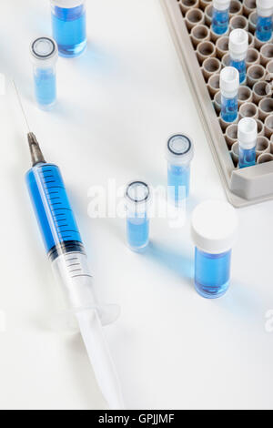 I flaconcini in un rack flaconcino e una siringa contenente un liquido di colore blu su un laboratorio di bianco sul banco di lavoro Foto Stock