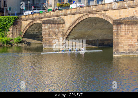 Quattro uomo canottaggio sculling una barca su un fiume in corrispondenza di un ponte Foto Stock