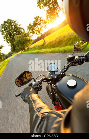 Conducente del motociclo equitazione sulla autostrada nella splendida luce del tramonto. Colpo da pillion vista driver Foto Stock