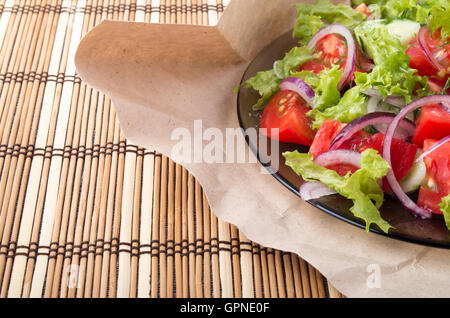 Primo piano su una piastra con insalata fresca di materie pomodori, lattuga e cipolla sullo sfondo della carta di avvolgimento e tappetino di bambù Foto Stock