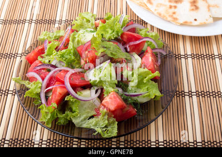 Close-up il piatto con una insalata di pomodoro a fette tagliate a fette, lattuga e cipolla in un marrone tappetino di bambù Foto Stock