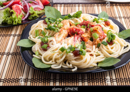 Primo piano la piastra nera con gli spaghetti e pezzi di stufato di pollo decorate con foglie di basilico e cipolle sul tavolo da pranzo è co Foto Stock