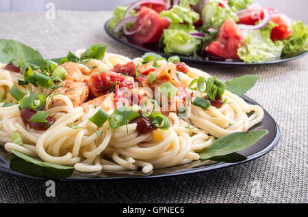 Home-pietanze cucinate su un tappetino grigio - spaghetti con i pezzi di pollo in umido e insalata di verdure con pomodori e lattuga Foto Stock
