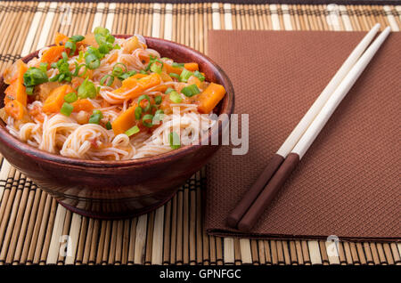 Piccola porzione di vermicelli di riso hu-teu con ragù vegetale di carote in un piccolo marrone ciotola di legno closeup sul tappeto a strisce vicino Foto Stock