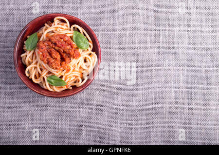 Vista dall'alto di un tappetino grigio con una piccola porzione di spaghetti cotti in una piccola ciotola di legno di colore marrone Foto Stock