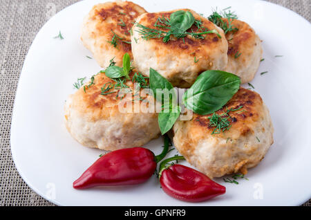 Vista ravvicinata sulla polpetta di pollo tritato su una piastra bianca con pepe rosso e basilico su un letto di sacco sullo sfondo Foto Stock