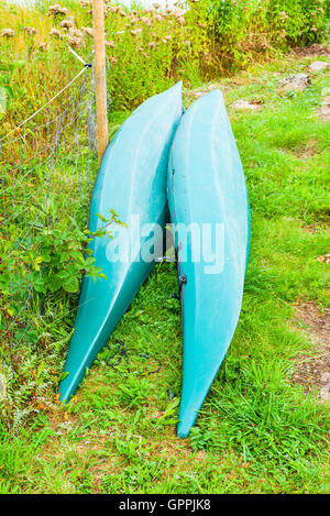 Due capovolto plastica canoe o kayak sulla terra asciutta. Le canoe sono verdi e lye accanto a un recinto reticolare accanto a una stretta walkwa Foto Stock