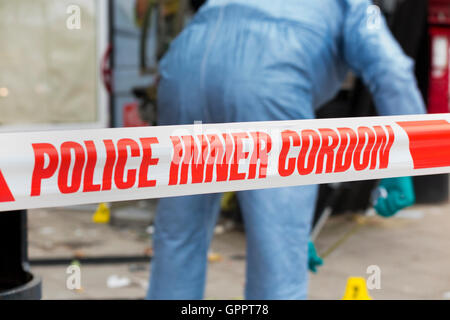 La polizia di cordone interno il nastro di barriera e una scena del crimine officer / ufficiali, & identificazione di prove marcatore numero / marcatori. Regno Unito Foto Stock