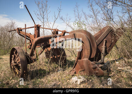 Vecchio di ferro arrugginito aratro abbandonato in un campo incolto. Foto Stock