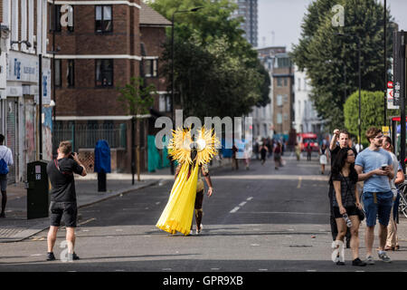 Donna che indossa il costume giallo al carnevale di Notting Hill in strada con le persone scattano fotografie Foto Stock