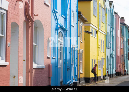 Viaggio in stile mare britannico, vista di una donna che indossa uno zaino che cammina tra le colorate case a schiera lungo il lungomare di Aldeburgh, Suffolk, Regno Unito. Foto Stock