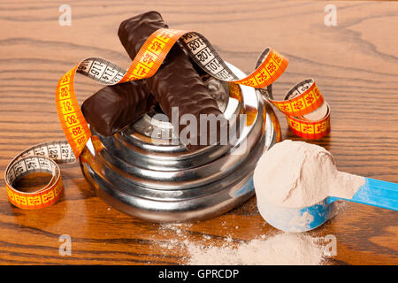 La proteina del siero di latte in polvere nel misurino, proteina bar, il metro a nastro e il manubrio su sfondo di legno. Foto Stock