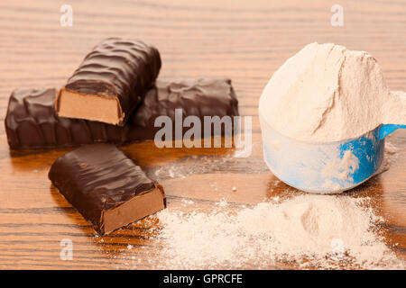 La proteina del siero di latte in polvere in misurino e proteina di cioccolato bar su sfondo di legno. Foto Stock