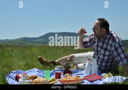 Uomo su picnic sta prendendo due ciliegie e portandoli vicino la sua bocca sulla giornata di sole Foto Stock