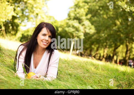 Giovane donna giacente in erba tenendo un arancione Foto Stock