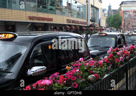 Una fila di taxi neri, taxi, con insegne luminose in attesa per i clienti su una trafficata High st Foto Stock