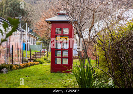 Uno stile vecchio telefono rosso stand in un paese erbosa lane Foto Stock