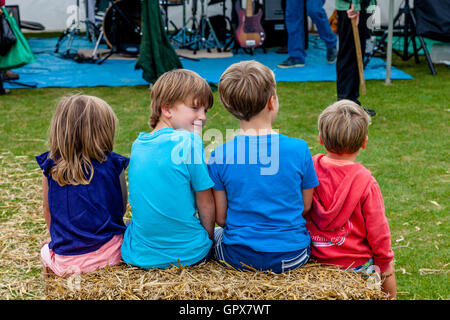 I bambini a sedersi su una balla di fieno in attesa per la Morris Ballerini per eseguire presso il Villaggio Hartfield Fete, Hartfield, East Sussex, Regno Unito Foto Stock