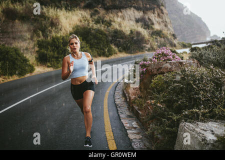A piena lunghezza shot della giovane donna fitness all'aperto in esecuzione su una strada aperta in campagna. Determinato atleta femminile in volata Foto Stock