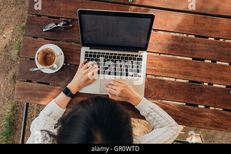 Vista superiore della femmina usando il suo computer portatile a un cafe'. Tettuccio di colpo di giovane donna seduta al tavolo con una tazza di caffè e mobile p Foto Stock