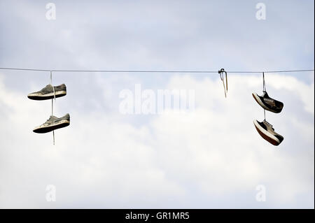 Due paia di scarpe posa su un cavo elettrico con cielo blu su sfondo Foto Stock