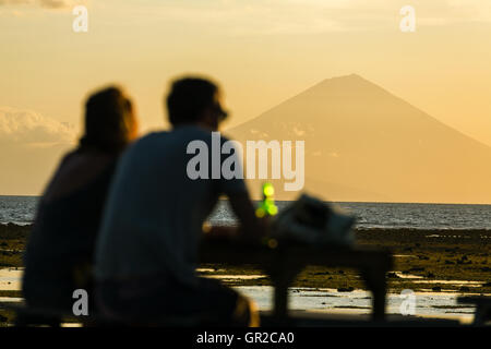 I turisti nel ristorante a Gili Travangan isola godendo di sera vista al tramonto sul Gunung Batur il vulcano di Bali, Indonesia. Foto Stock