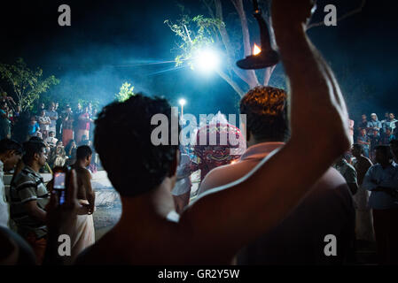 Un uomo detiene una fiamma aloft per illuminare i lavori a un rituale theyyam in una regione del nord del Kerala village vicino a Kannur Foto Stock