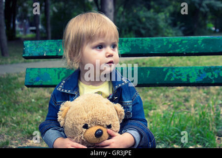 Bambino seduto sulla panchina del parco Foto Stock