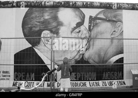 Una ragazza che sta fissando i graffiti di baciare sul muro di Berlino. Foto Stock