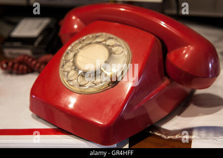 Telefono con teleselezione rotante rossa degli anni '70 su una scrivania completa di carte Foto Stock