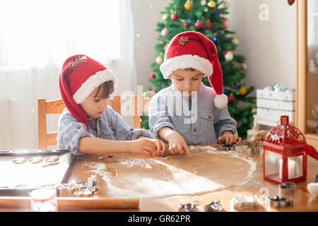 Due simpatici ragazzi con santa hat, preparazione di biscotti a casa, albero di Natale dietro di loro Foto Stock