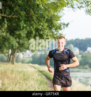 Atletica Giovane uomo a fare jogging nel parco di mattina. Formazione in esecuzione all'esterno con spazio di copia Foto Stock