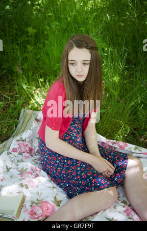 Bella ragazza seduta su una coperta in un prato con un libro Foto Stock