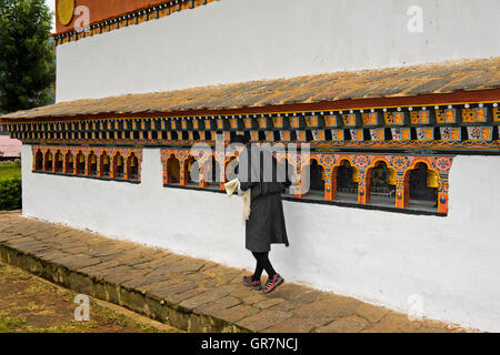 Giovane uomo locale girando la preghiera Mills, Monastero Chime Lhakhang vicino Lobesa, Bhutan Foto Stock