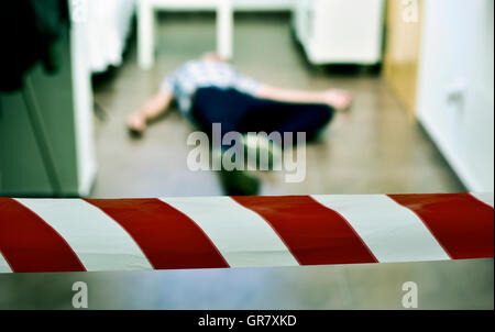 Dettaglio di una scena del crimine con il corpo morto di un giovane uomo disteso sul pavimento all'interno con un punto rosso e bianco il nastro della polizia in fo Foto Stock